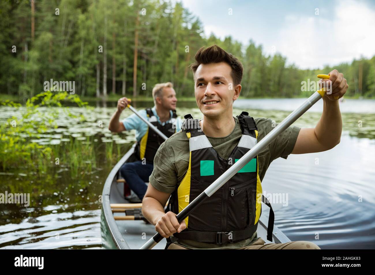 Zwei Männer im Leben haben Kanufahren im Waldsee. Wasseroberfläche mit Seerosen bedeckt. Touristen, die in Finnland reisen und Abenteuer erleben. Stockfoto