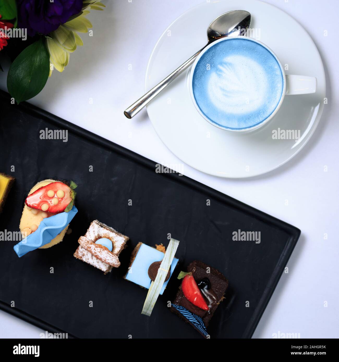 Tasse vegan blue Latte und kleinen Leckereien. Konzept der trendigen Koffein frei vegan Erfrischungspause. Ansicht von oben. Mini desserts Sammlung. Weißer Hintergrund. Platz Stockfoto