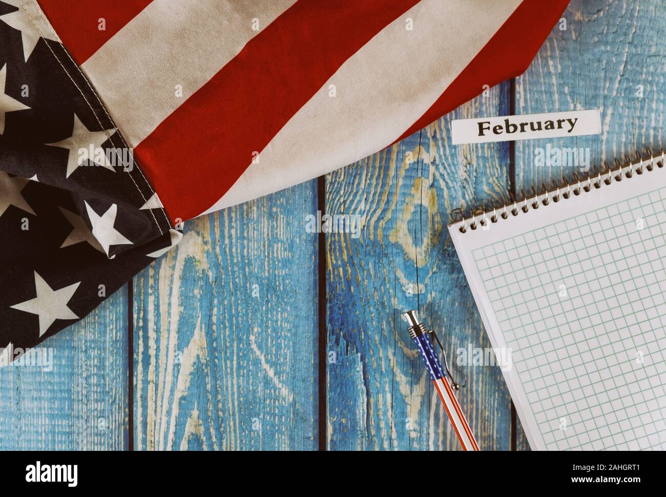 Februar Monat Kalenderjahr Vereinigte Staaten von Amerika Flagge der Freiheit und der Demokratie mit leeren Notizblock und Stift auf Office alte blaue Holztisch Stockfoto