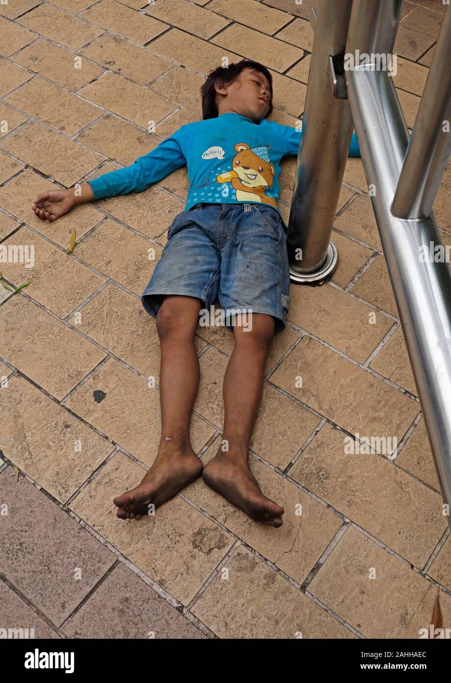Jakarta, Indonesien - 2019.12.16: Ein kleiner Junge Kind schlafen auf dem Gehsteig vor Grand Indonesia Shopping Mall in der Innenstadt Stockfoto