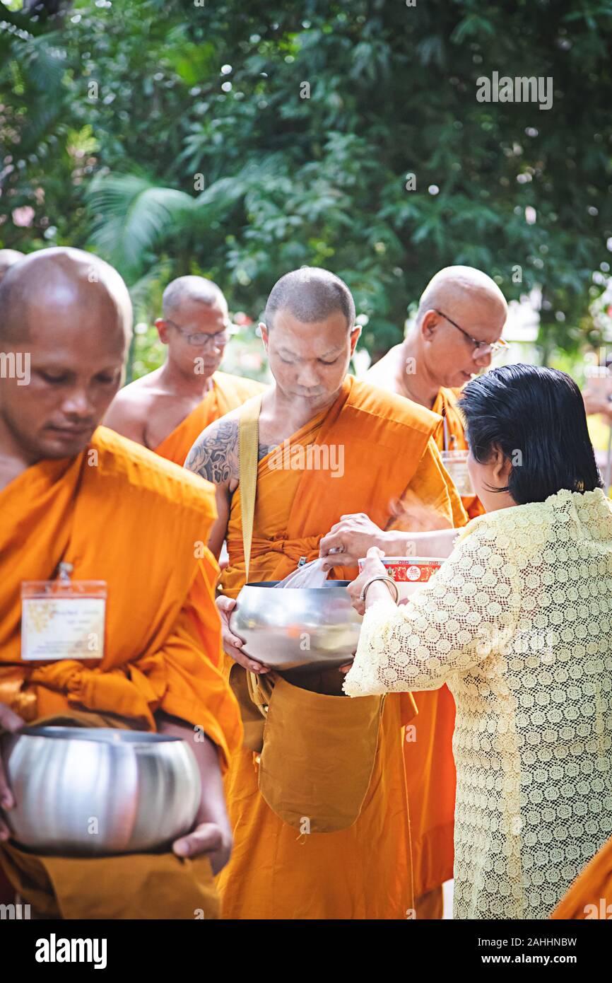 Phuket - Thailand, 7. Mai 2019: Viele thailändische Mönch mit Almosen Schüssel, während alte Dame mit Speisen in die Schüssel, die heißer Rauch Fluss bis in den Morgen Zeit Stockfoto