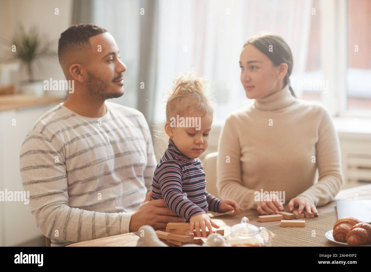 In warmen Tönen Porträt des modernen Mixed-race Familie an jedem anderen Suchen, beim Spielen mit niedlichen Tochter zu Hause Stockfoto