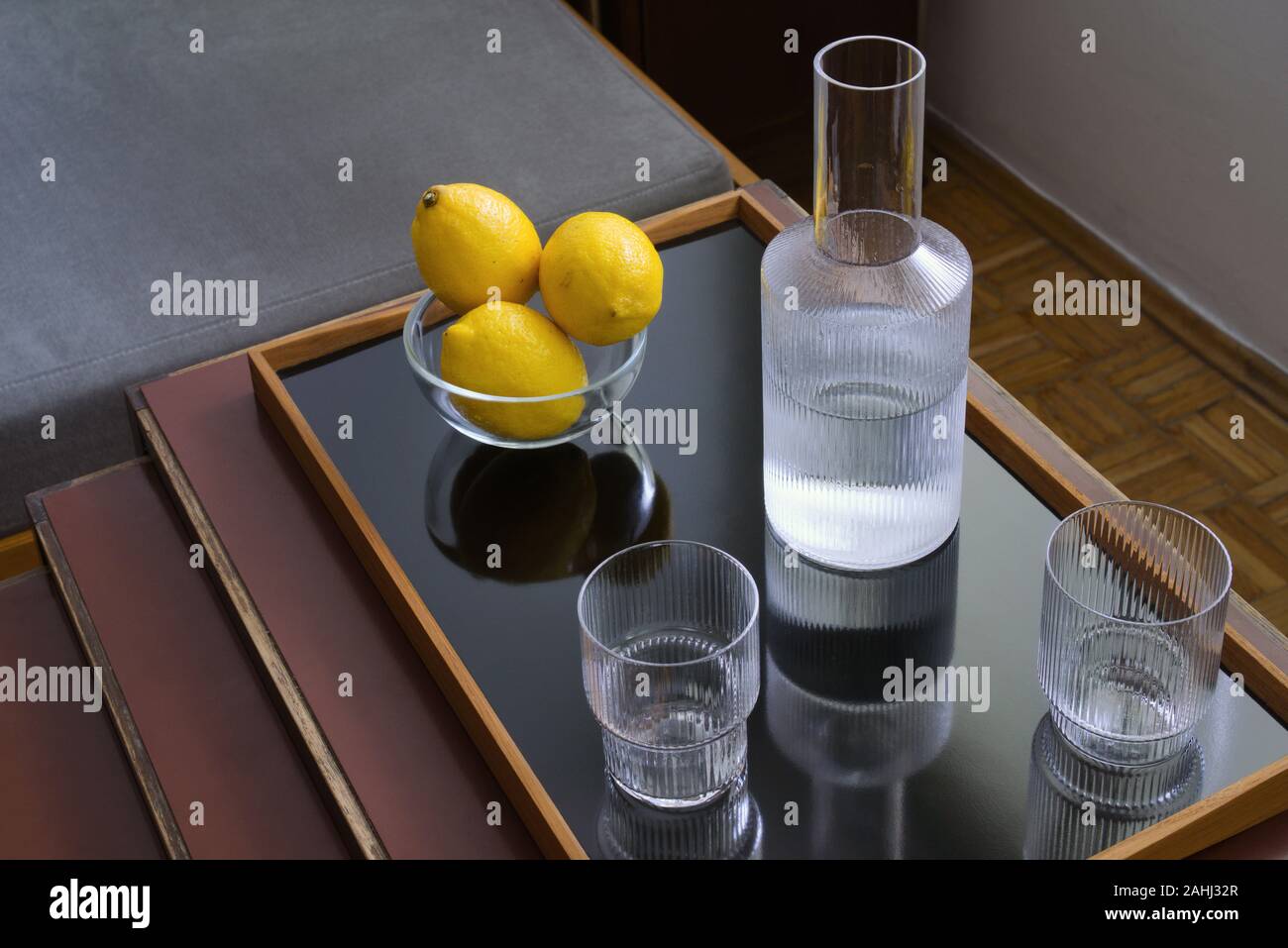 Drei frische gelbe Zitronen in ein Glas Schale, zwei Gläser und Karaffen mit Wasser auf modernen Fach auf Tabelle, noch Leben Stockfoto
