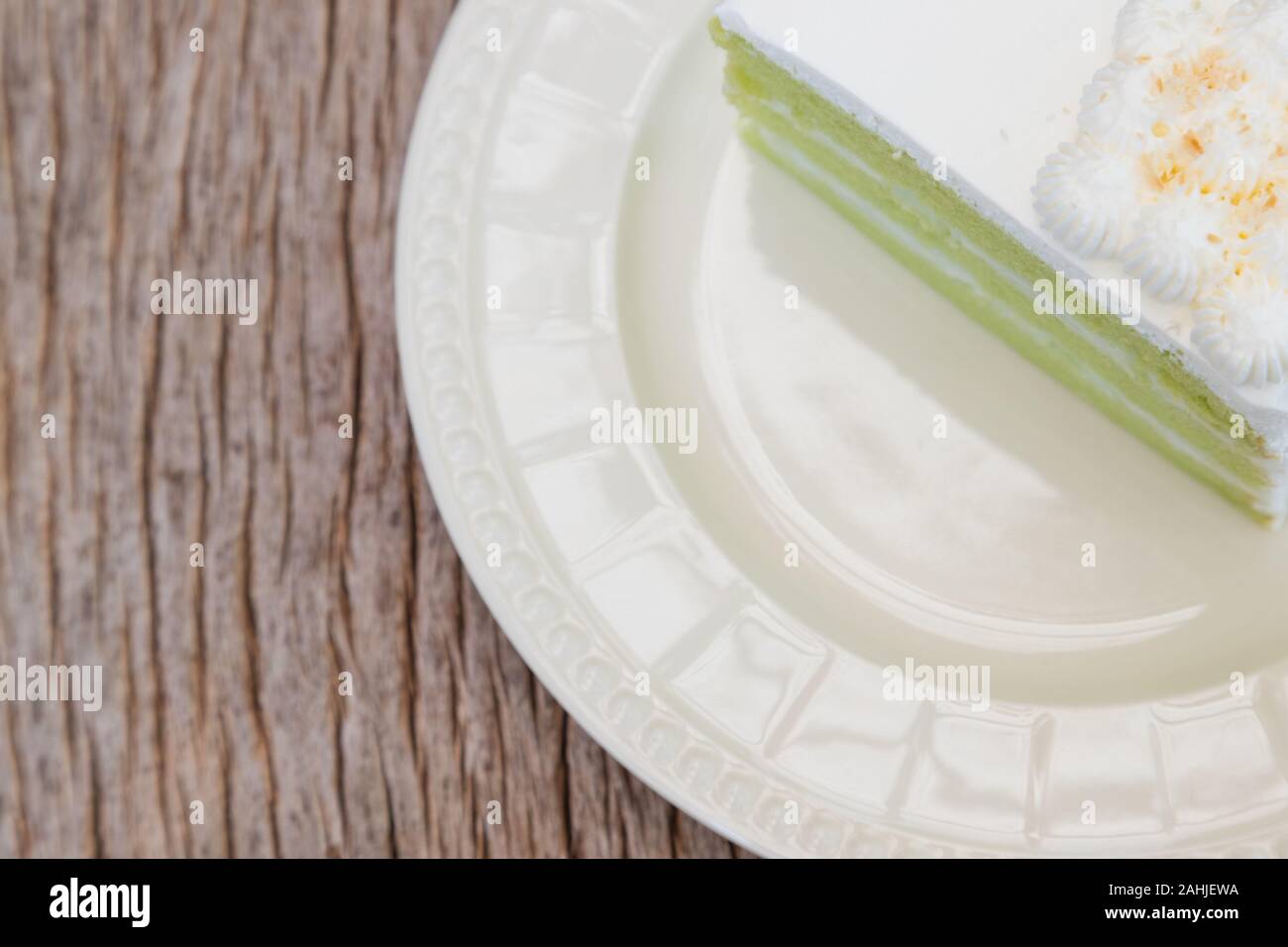 Closeup weichen, grünen Kokoscreme Kuchen in einem Stück auf sauberen Teller am Rande für Raum, auf der Rinde, Holz- Textur Tisch Stockfoto