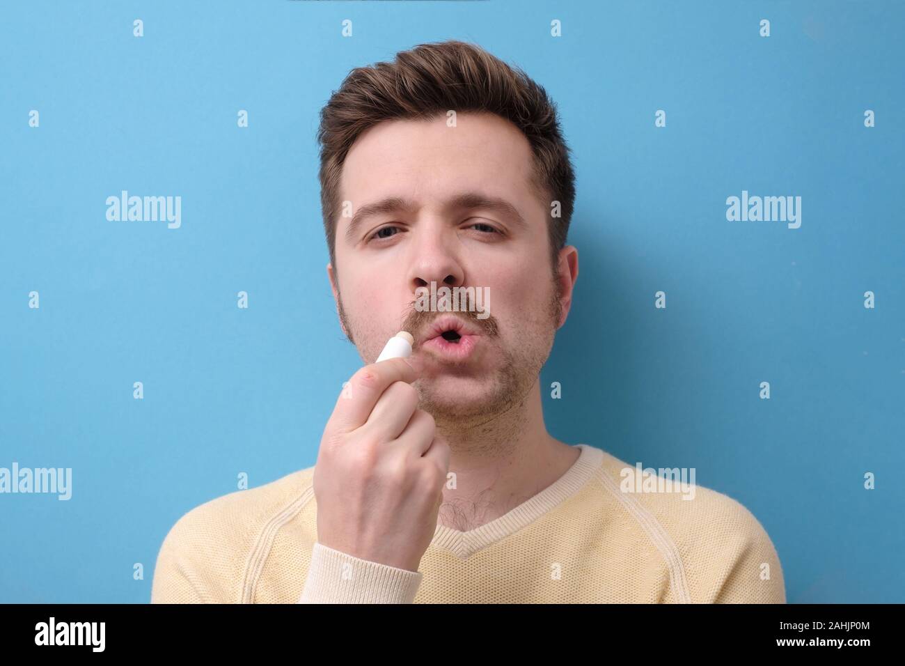Guy Anwendung Balsam auf Risse trockene Lippen mit hygienischen Balsam auf blauem Hintergrund isoliert Stockfoto
