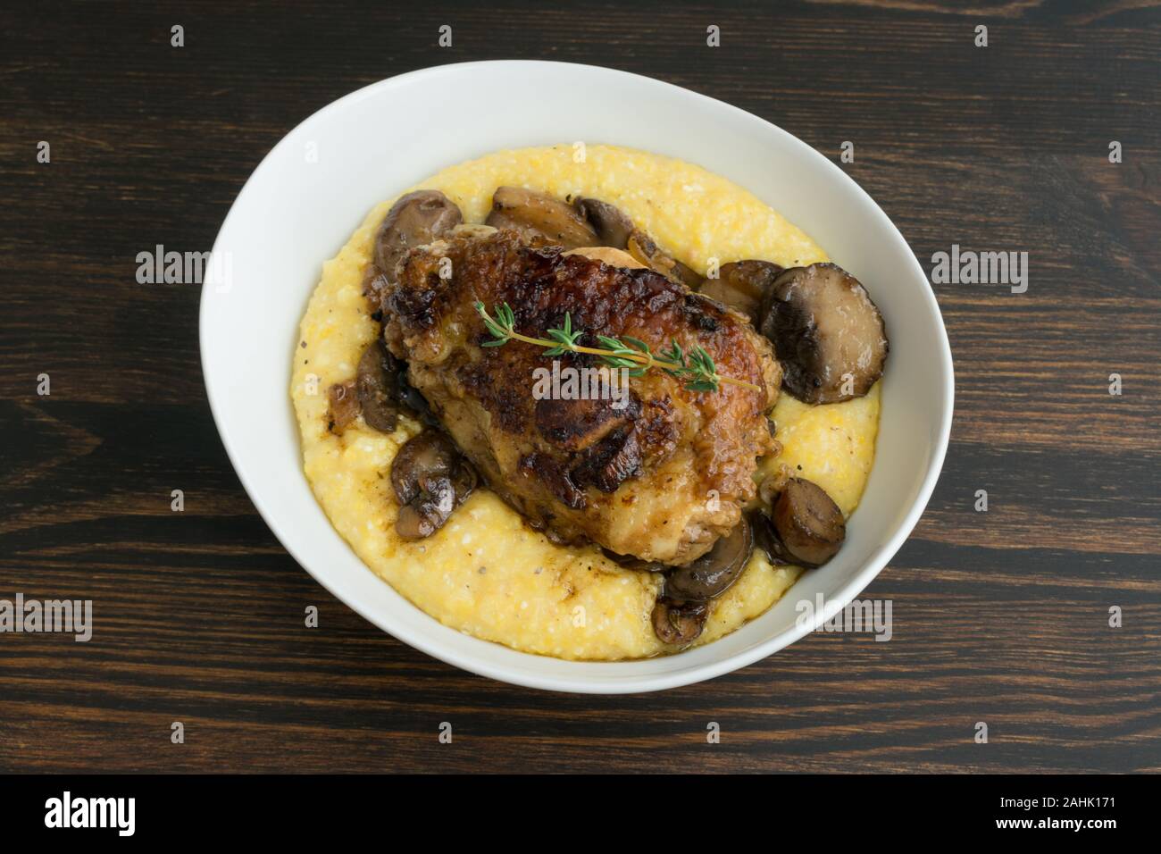 Geschmorte Hühnerkeule mit Pilzen und cremiger Polenta: cremiger Polenta überbacken mit in Scheiben geschnittenen Champignons und ein Geschmortes Hähnchen Schenkel Stockfoto