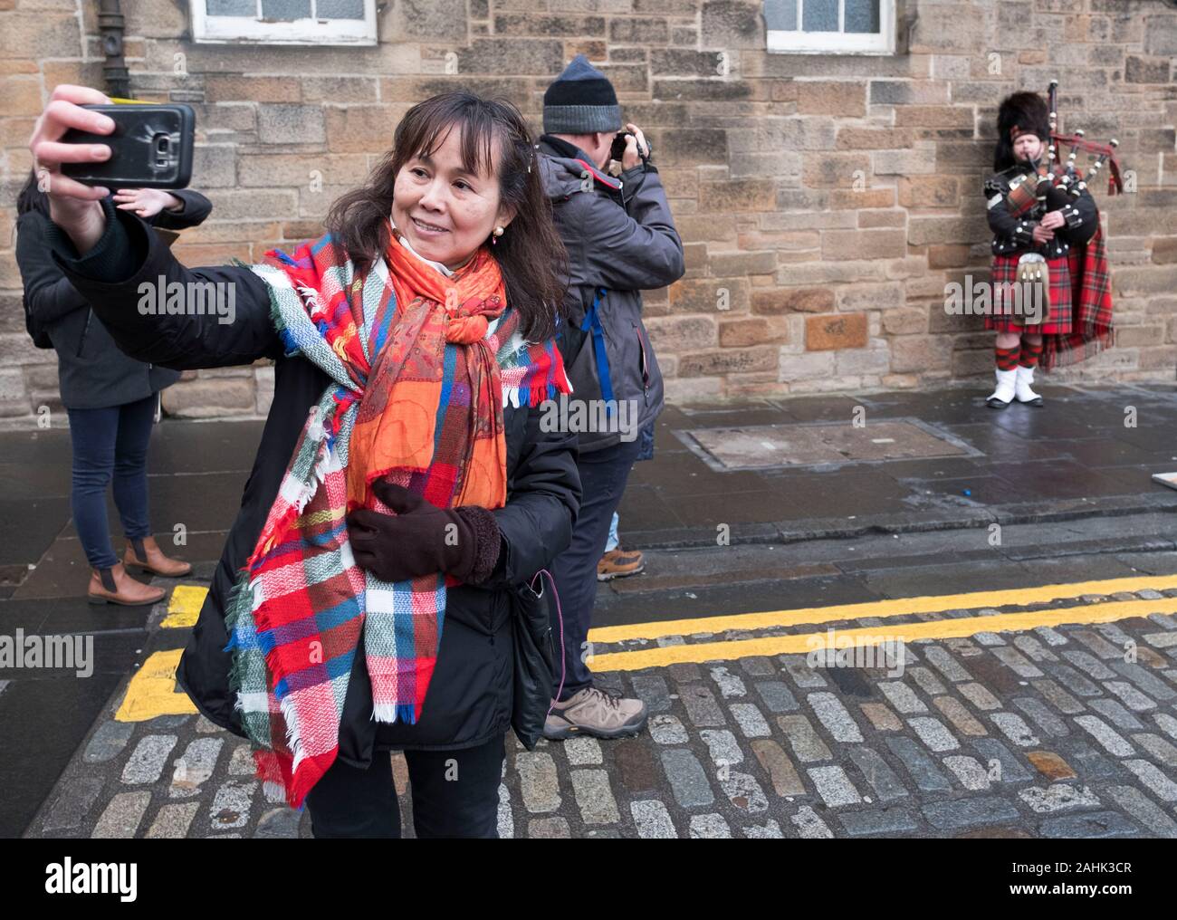 Touristen fotografieren einer Piper Straßenmusik auf der Royal Mile, Edinburgh, Schottland. Stockfoto