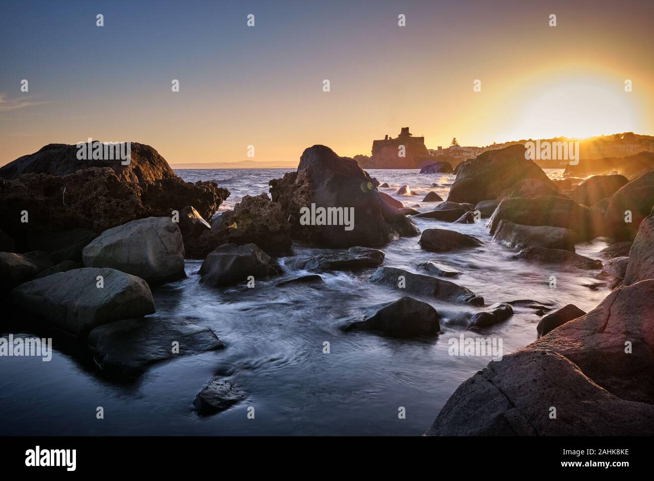 Sonnenuntergang über Aci Castello mit Wellen über die Felsen im Vordergrund brechen, Catania, Italien Stockfoto