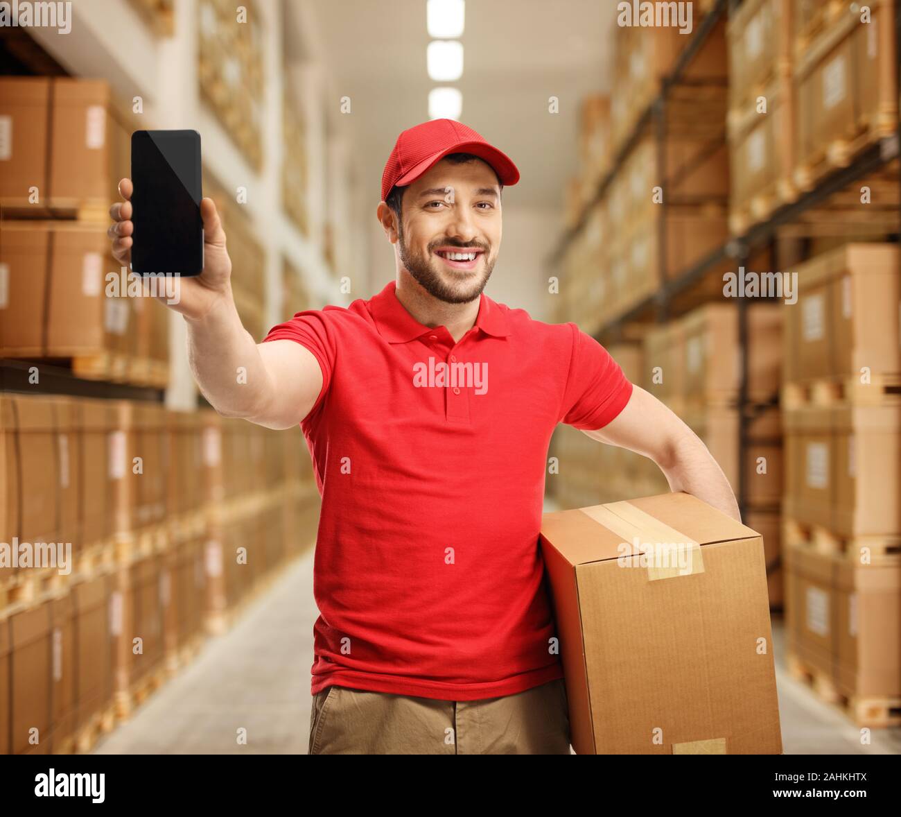 Lieferung Kerl halten sie ein Paket und zeigt ein Mobiltelefon in einem Lager Stockfoto