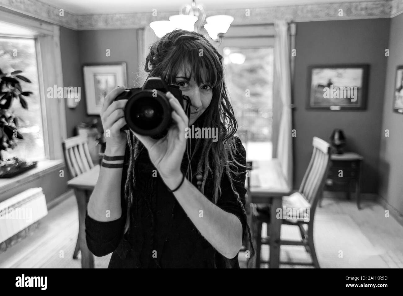 Schwarze und weiße Nahaufnahme Portrait von professionellen Fotografen hand-Holding eine DSLR-Kamera. Natürlich schönes Mädchen mit Dreadlocks und Tätowierungen. Stockfoto