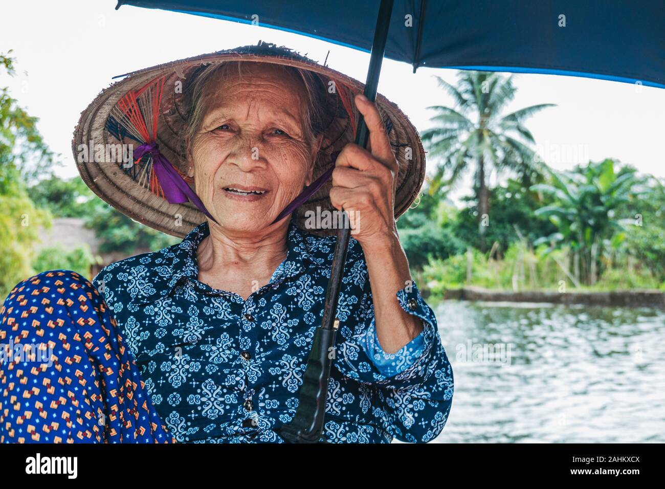 Eine ältere Frau mit ihren Füßen die Ruder der ein Ruderboot zu drücken, während Sie einen Ventilator und Regenschirm, die Touristen die Ngo Dong Fluss, Vietnam Stockfoto
