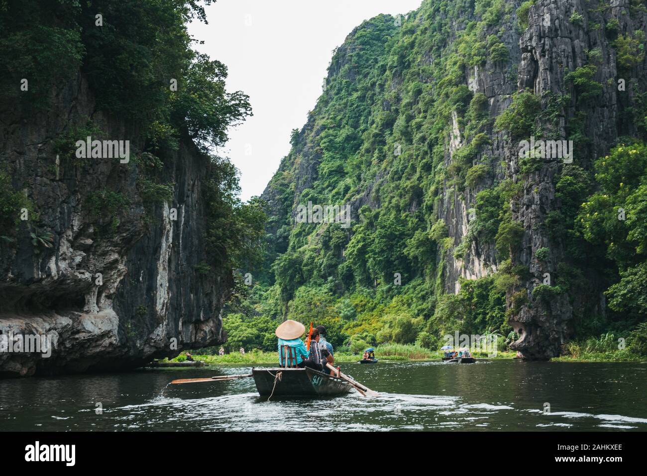 Touristen in Boote Zeile nach oben Die Ngo Dong Fluss durch Kalkstein Berge und Höhlen in der Tam Coc, Provinz Ninh Binh, Vietnam Stockfoto