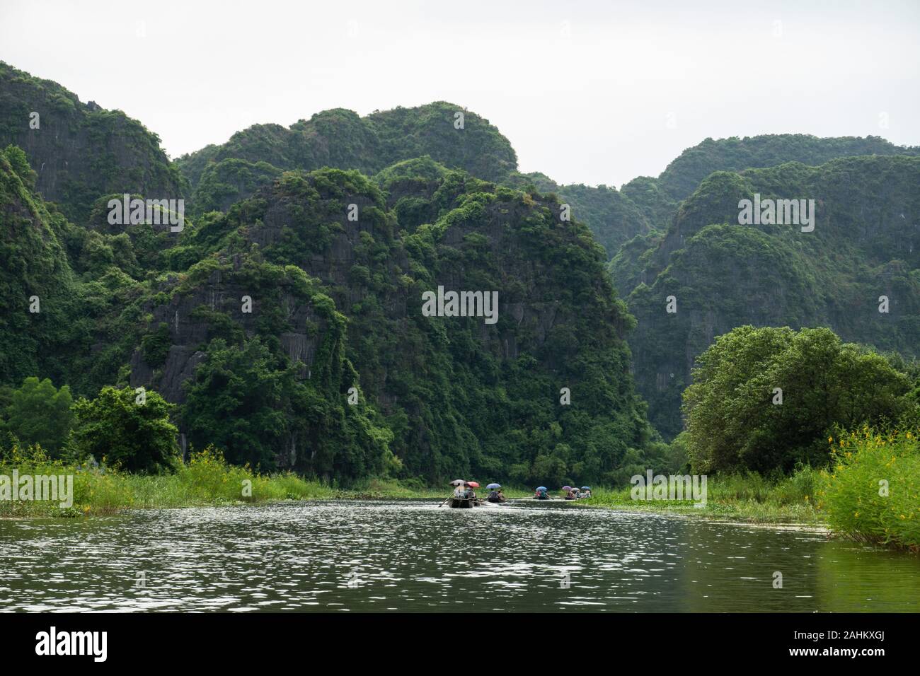 Touristen in Boote Zeile nach oben Die Ngo Dong Fluss durch Kalkstein Berge und Höhlen in der Tam Coc, Provinz Ninh Binh, Vietnam Stockfoto