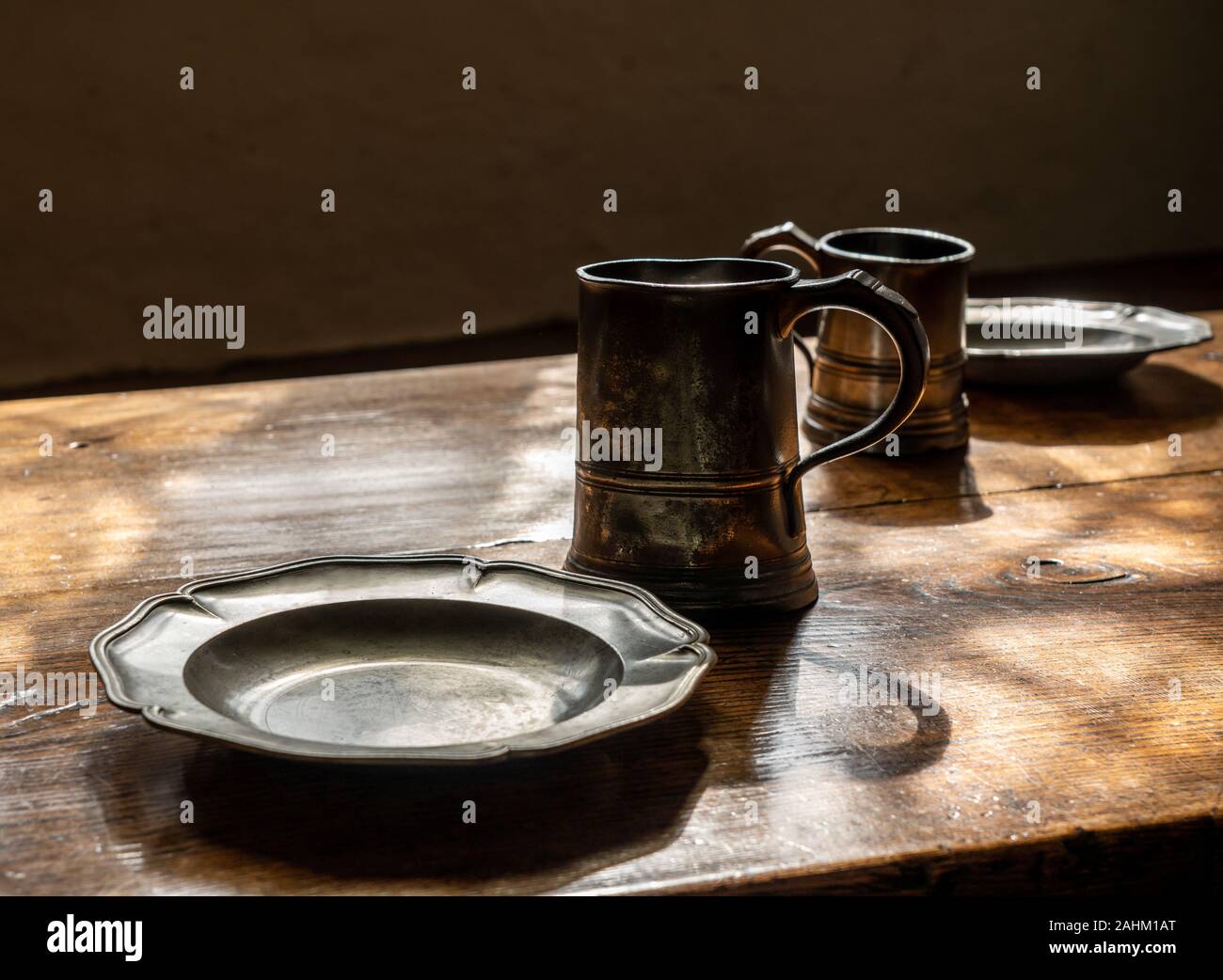 Antike Zinn trinken Becher und flachen Tellern mit kein Essen am großen Esstisch aus Holz Stockfoto