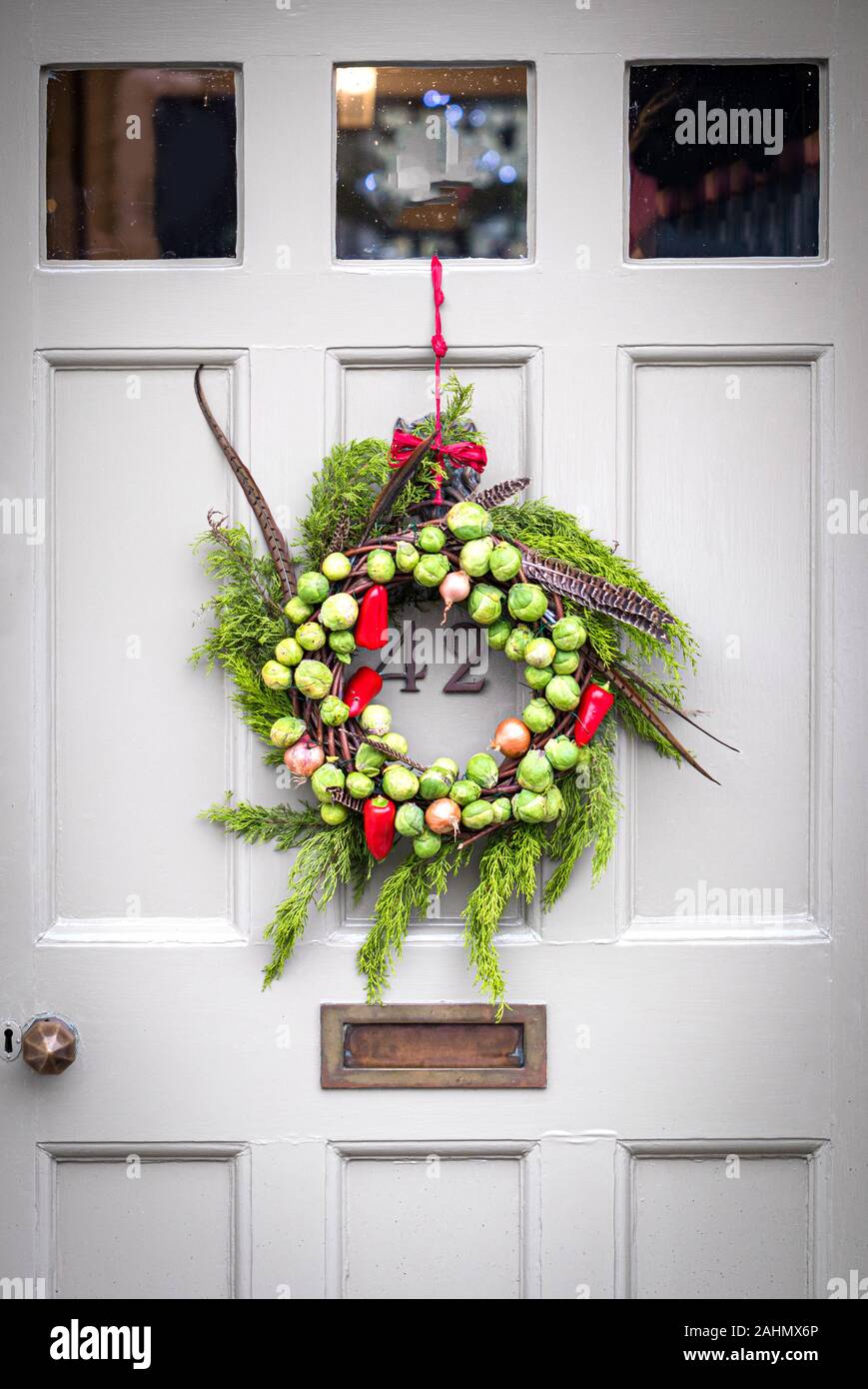 Decorateive festliche handgefertigte Gemüse Kranz von Rosenkohl, Zwiebeln, Chili, immergrünen Blätter und Fasan Federn hängen an eine alte Tür gemacht Stockfoto