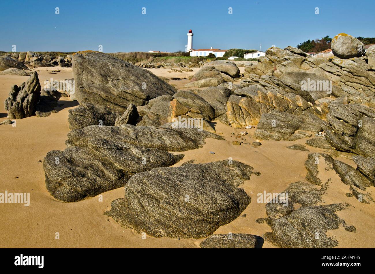 Küste Steine im Osten der Insel Yeu mit Sand umgeben und der Leuchtturm am Pointe des Corbeaux im Hintergrund ist Stockfoto