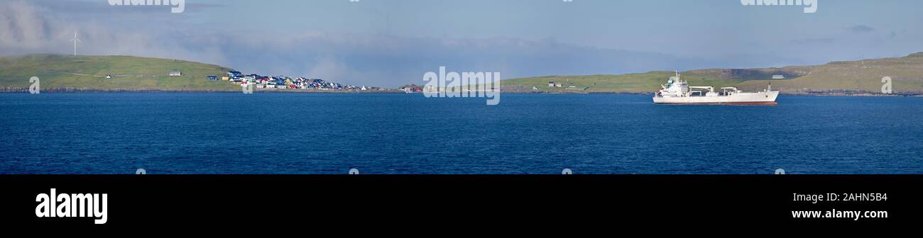 Panoramablick auf die Insel Nolsoy ang Dorf der Färöer Inseln, Gewässern des Atlantik und fahrendes Schiff sind im Vordergrund Stockfoto