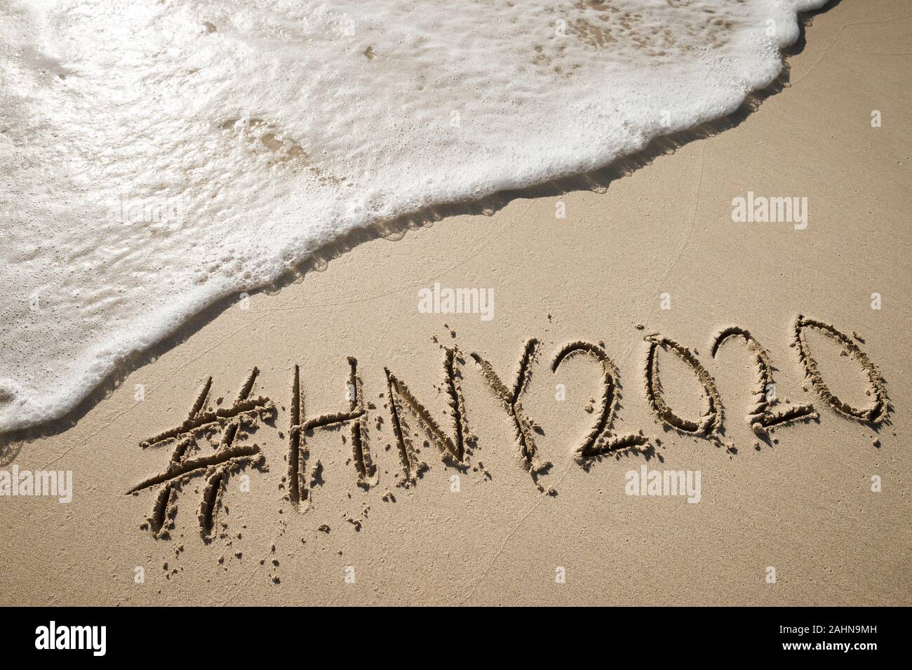 Modernes neues Jahr Nachricht mit social media Hashtag für 2020 handschriftlich in sanften Sand mit entgegenkommenden Wellen am Strand Stockfoto