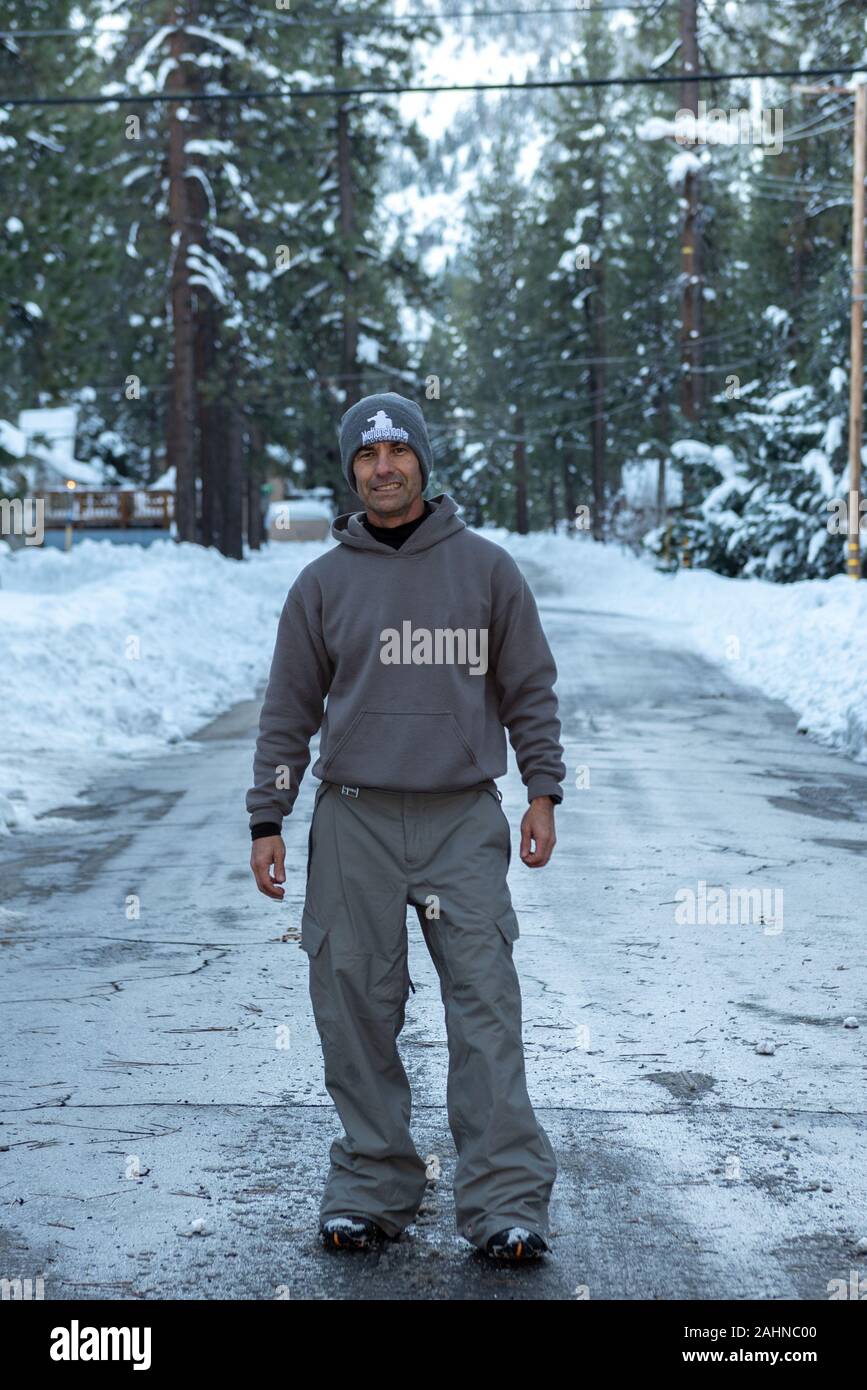 Mittleres Alter asiatischen amerikanischen Mann steht auf einem gefrorenen und gepflügt Straße in gekleidet für kaltes Wetter in die verschneite Umgebung von wrightwood. Stockfoto