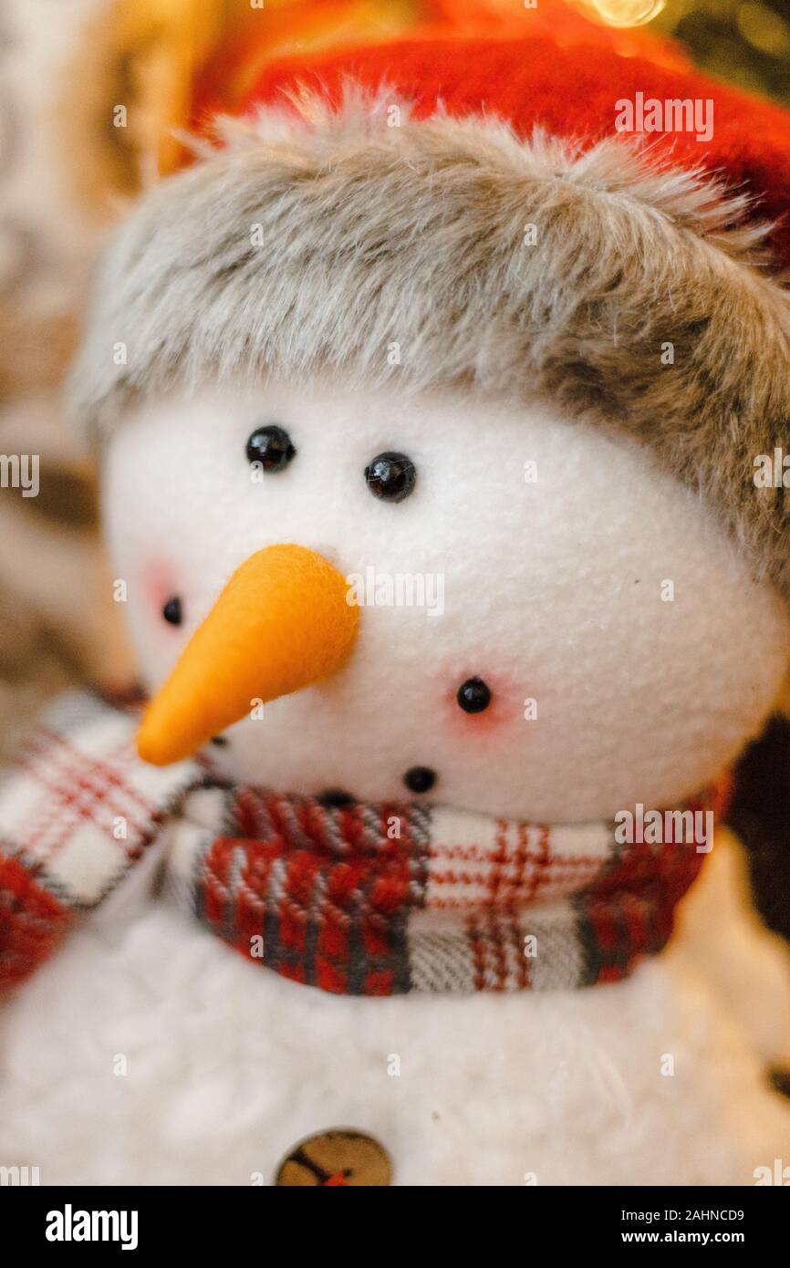 Porträt eines Schneemannes Stofftier Plüsch lächelnd mit Santa Hut, roter Schal, orange Karotte Nase mit Weihnachtsbaum im blurry bokeh Hintergrund Stockfoto