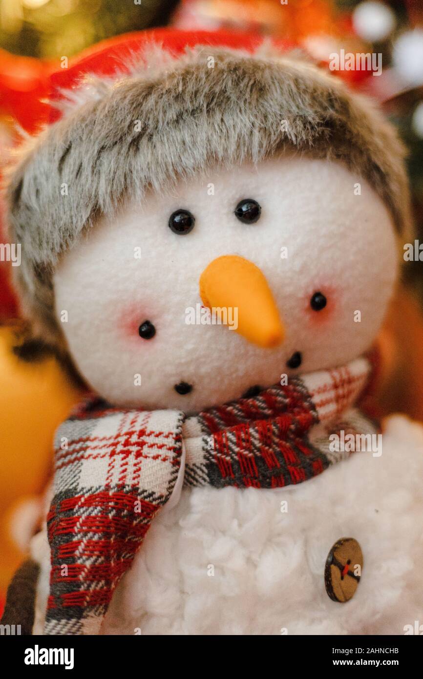 Porträt eines Schneemannes Stofftier Plüsch lächelnd mit Santa Hut, roter Schal, orange Karotte Nase mit Weihnachtsbaum im blurry bokeh Hintergrund Stockfoto
