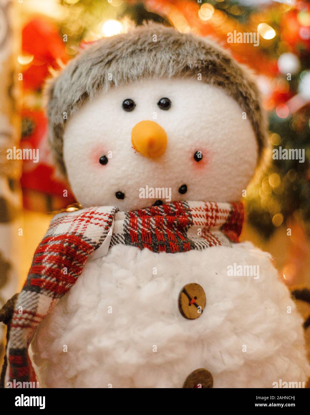 Porträt eines Schneemannes Stofftier Plüsch lächelnd mit Santa Hut, roter Schal, orange Karotte Nase mit Weihnachtsbaum im blurry bokeh Hintergrund Stockfoto