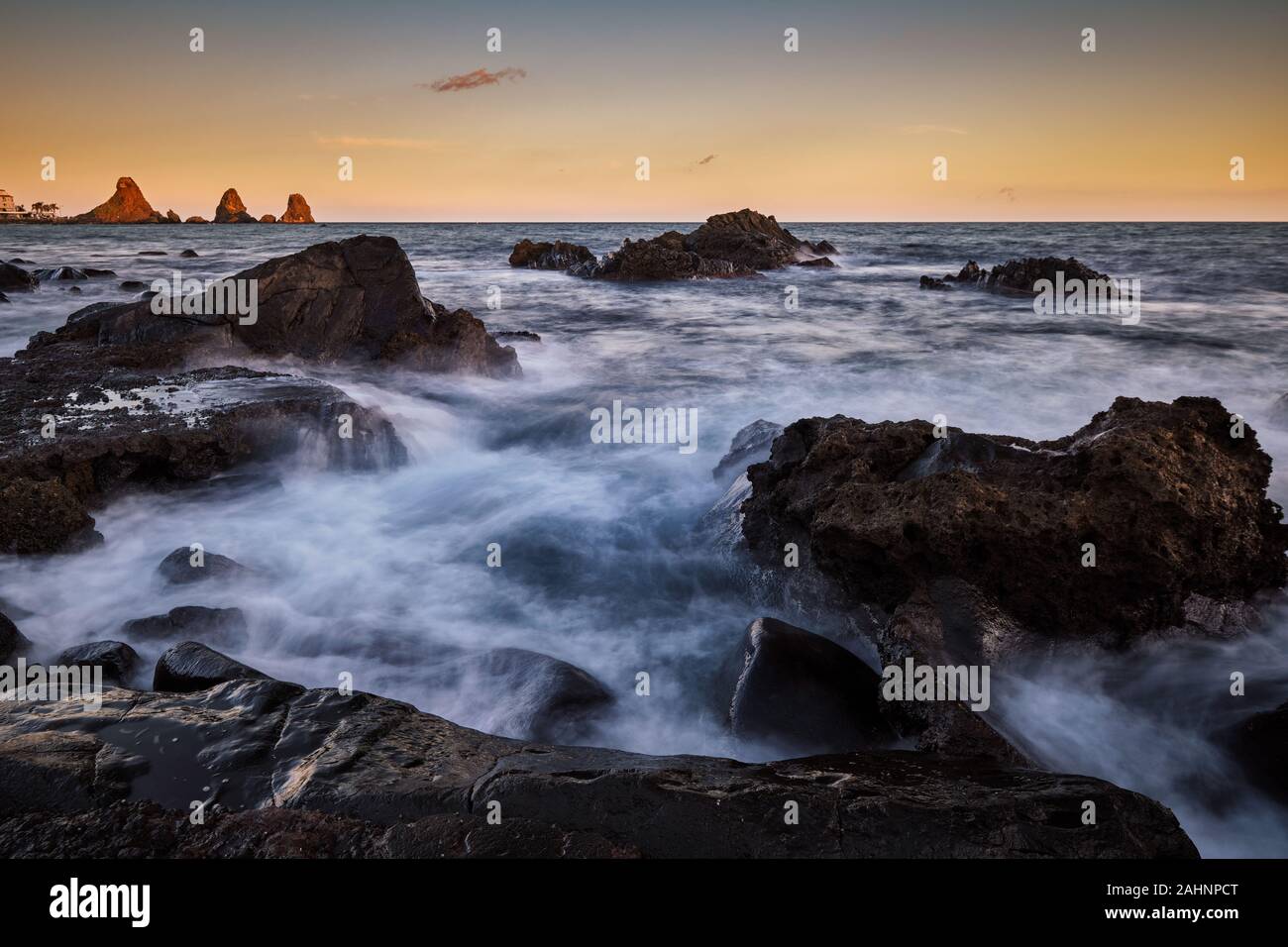 Sonnenuntergang über Aci Trezza und Ihre sea Stacks mit Wellen über die Felsen im Vordergrund brechen, Catania, Italien Stockfoto