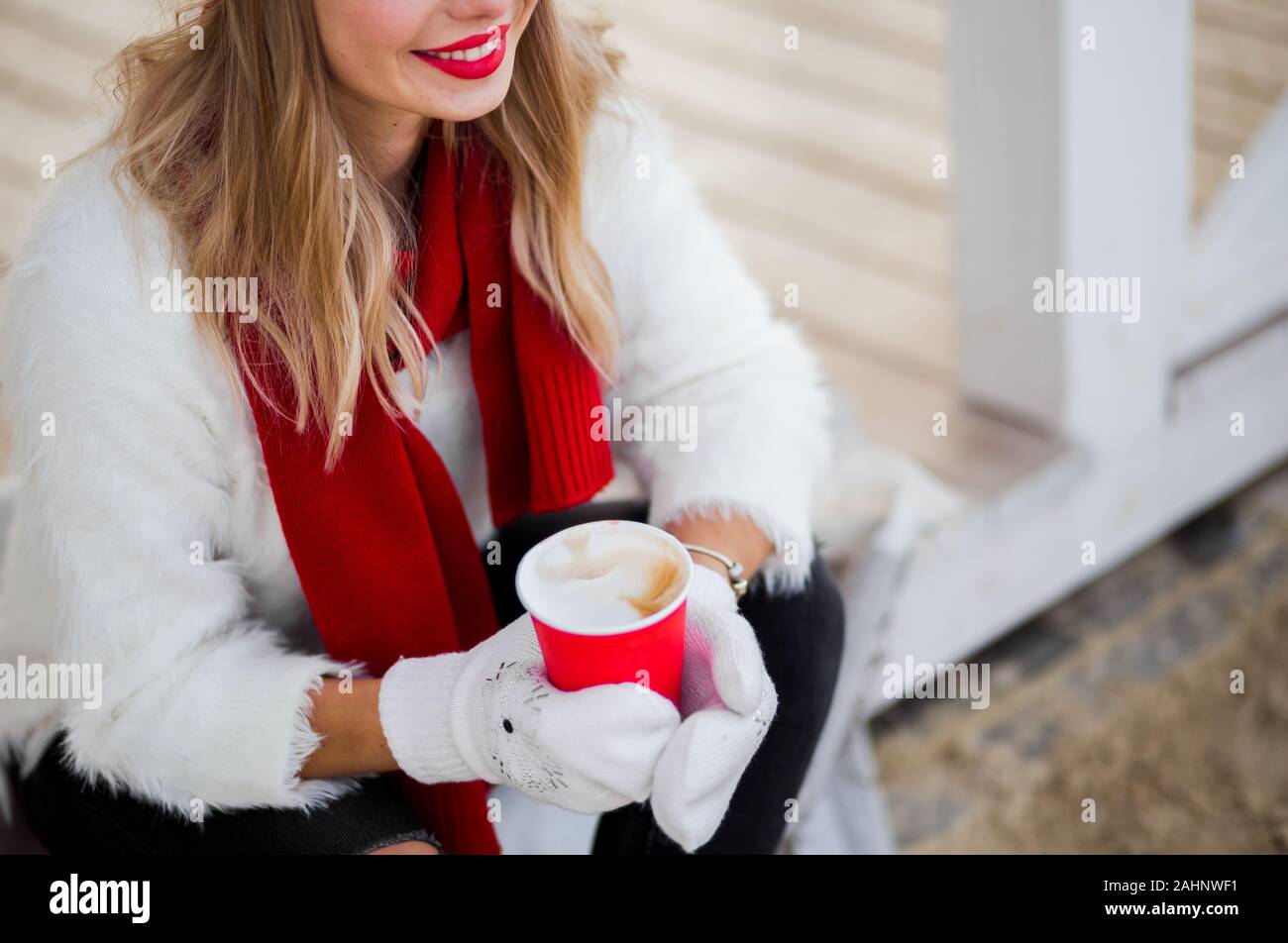 Frau mit heißen Getränk in die Hände in Handschuhe in weißen flauschigen pullover, rot Schal und grauen Hut. Stockfoto