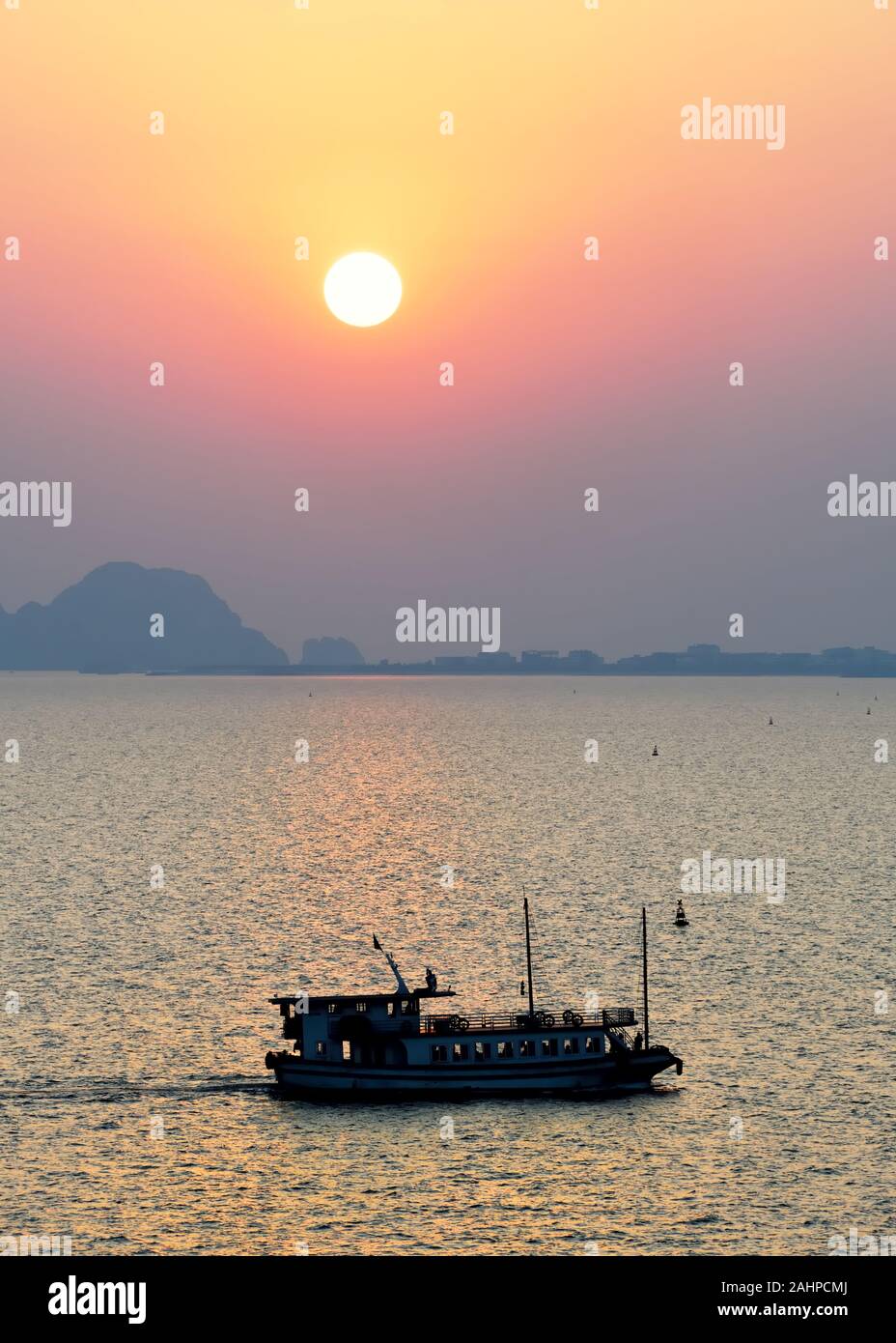 Die Sonne, die durch die niedrigen Dunst in Ha Long Bay als Junk-boot Köpfe für zu Hause im Nordosten von Vietnam. Stockfoto