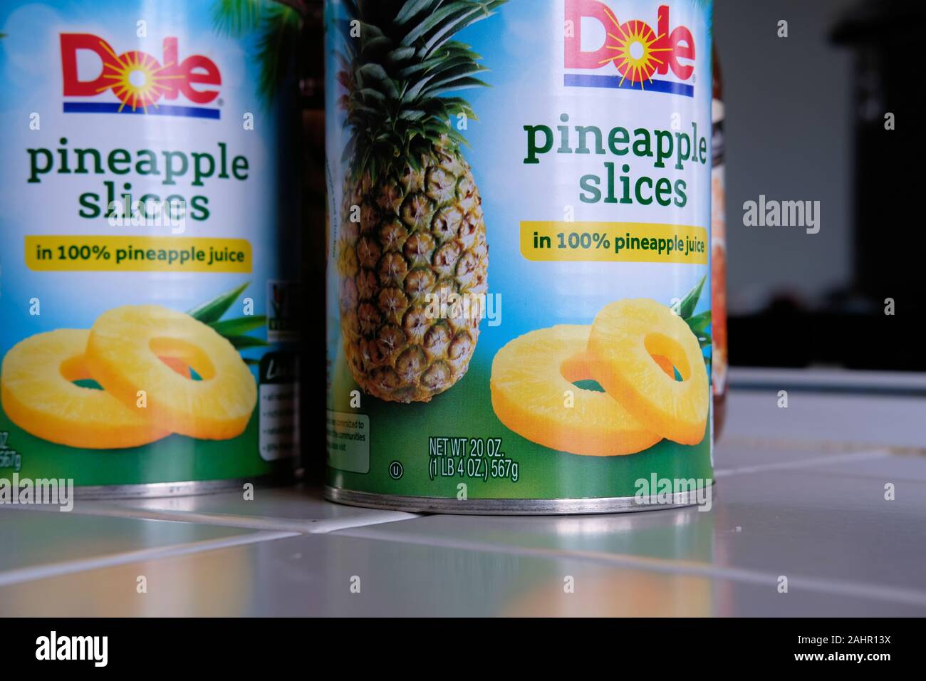 Zwei 20 Unze Blechdosen (567 Gramm) von Dole Marke Ananasscheiben in 100% Ananas Saft auf eine geflieste Küche begegnen. Stockfoto