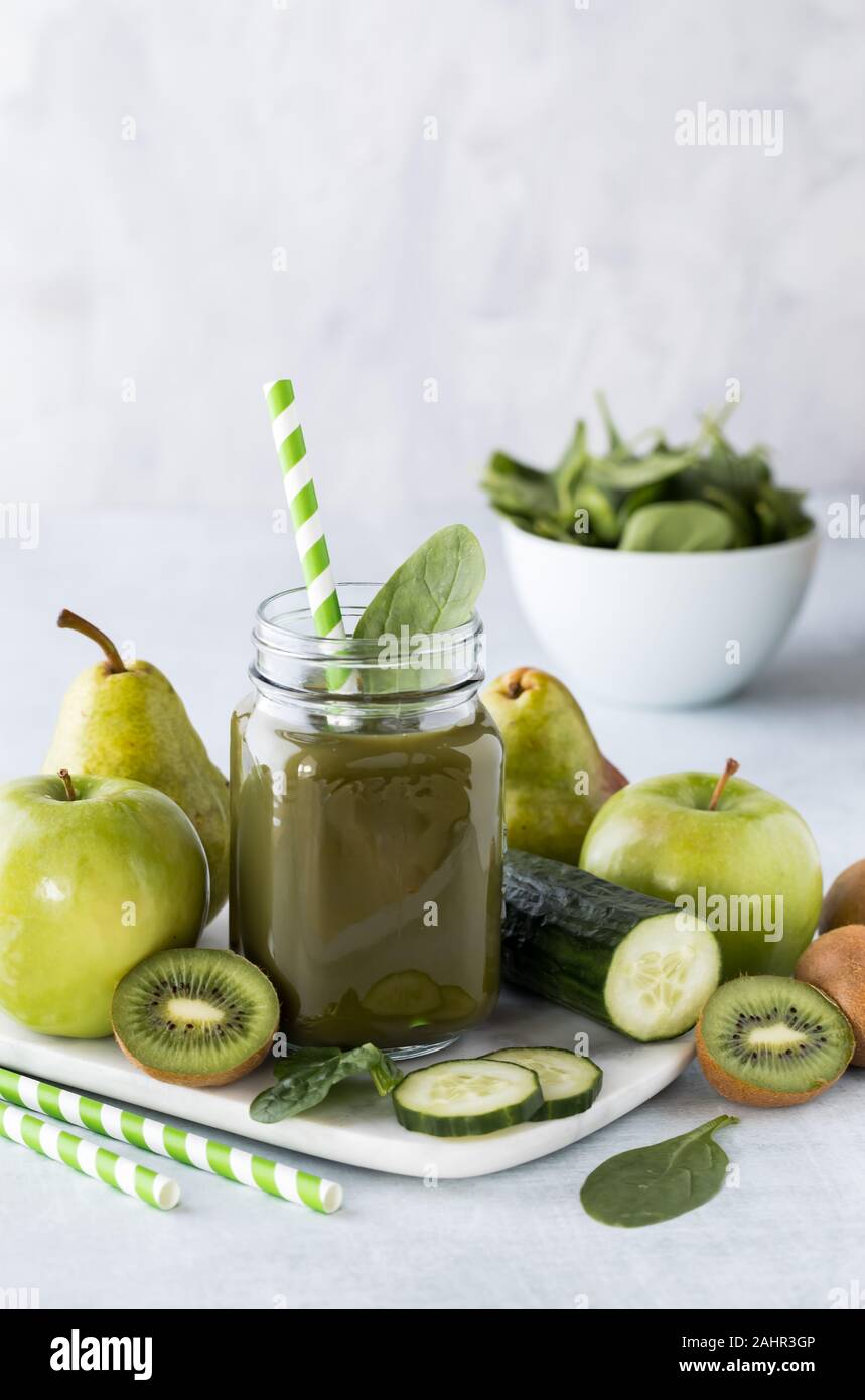 Eine Nahaufnahme von einem Glas mit grüner Smoothie von grünen Früchten und Gemüse und eine Schüssel mit Spinat im Hintergrund umgeben gefüllt. Stockfoto