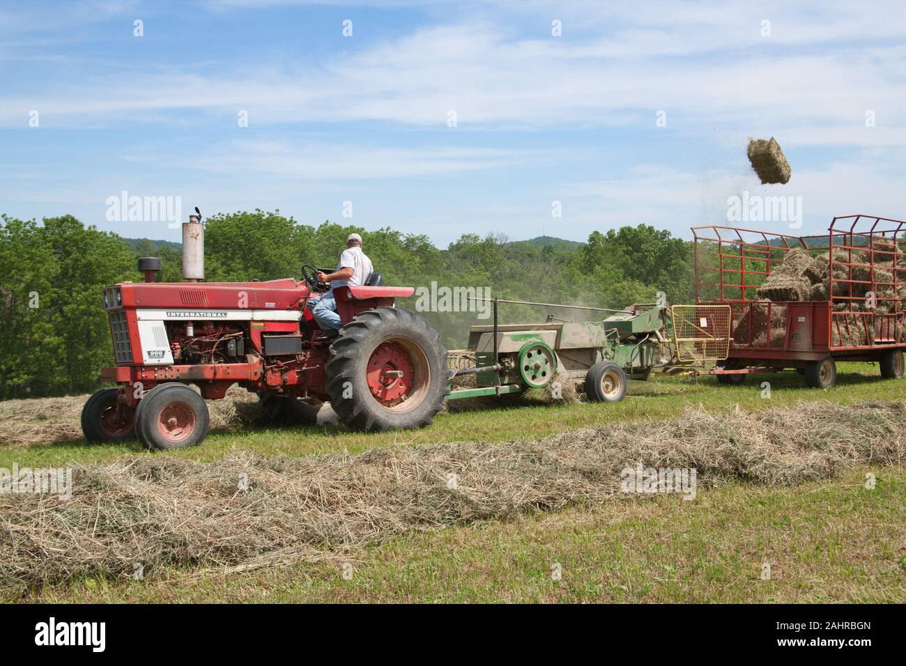 Mann auf International Harvester Farmall Traktor, Pressen von Heu in einem Feld mit einem Ballen fliegen in die Luft, in Lincoln, Illinois, USA. (Für die redaktionelle Nutzung onl Stockfoto