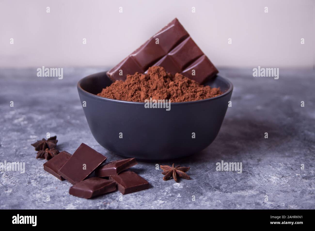 Schüssel mit Kakaopulver und Stücke Schokolade auf dem grauen Hintergrund. Stockfoto