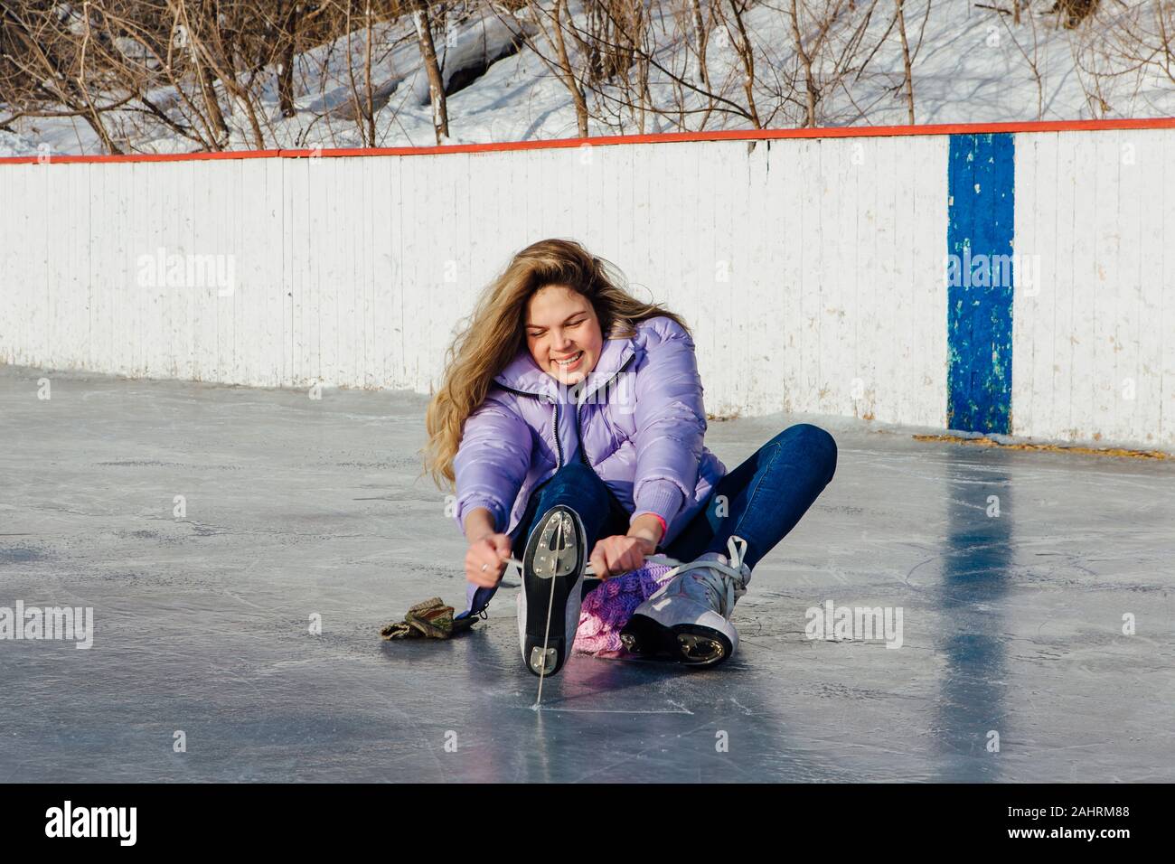 Reizende junge Frau sitzt auf der Eisbahn und tieing Schnürsenkel Stockfoto