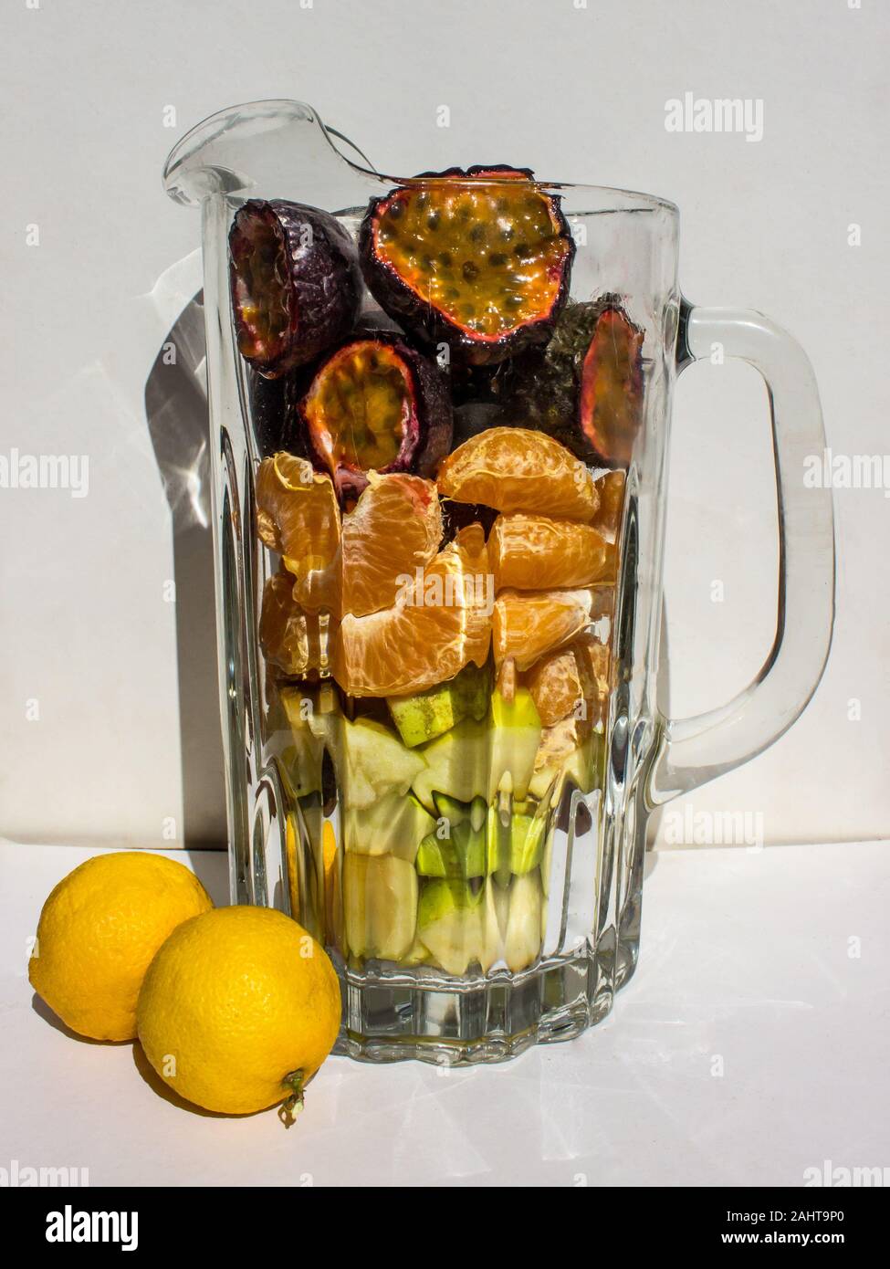Verschiedene Arten von Früchten wie Passionsfrucht, Mandarinen und Äpfel in einem Glas Mug vor einem weißen Hintergrund Stockfoto