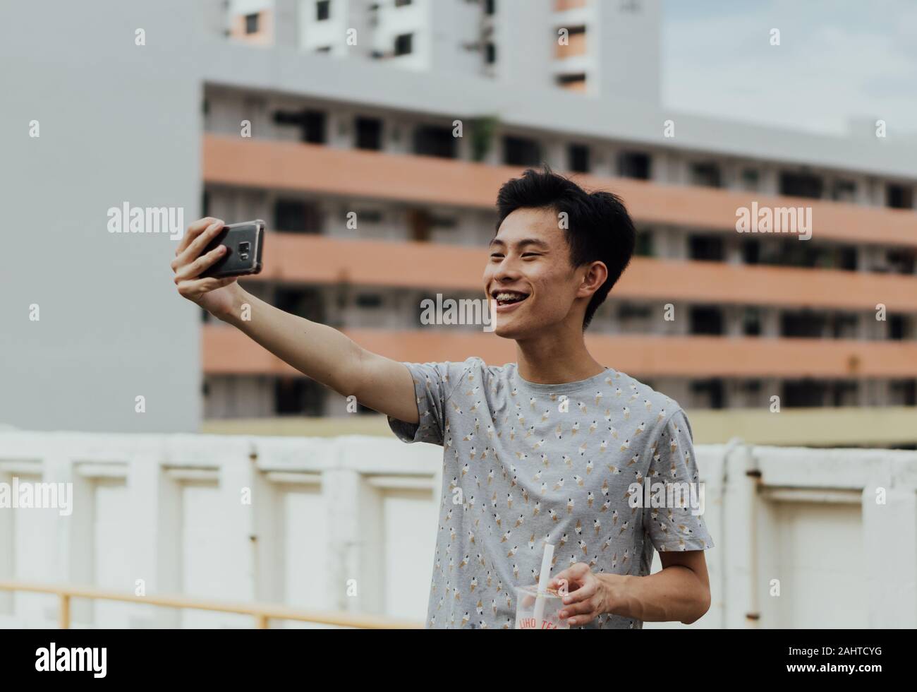Asiatischer männlicher Vlogger, der authentische Chinatown, Singapur-Erfahrung mit Smartphone, HDB-Gehäuse im Hintergrund, Content Creator, Street Vlogging erfasst Stockfoto