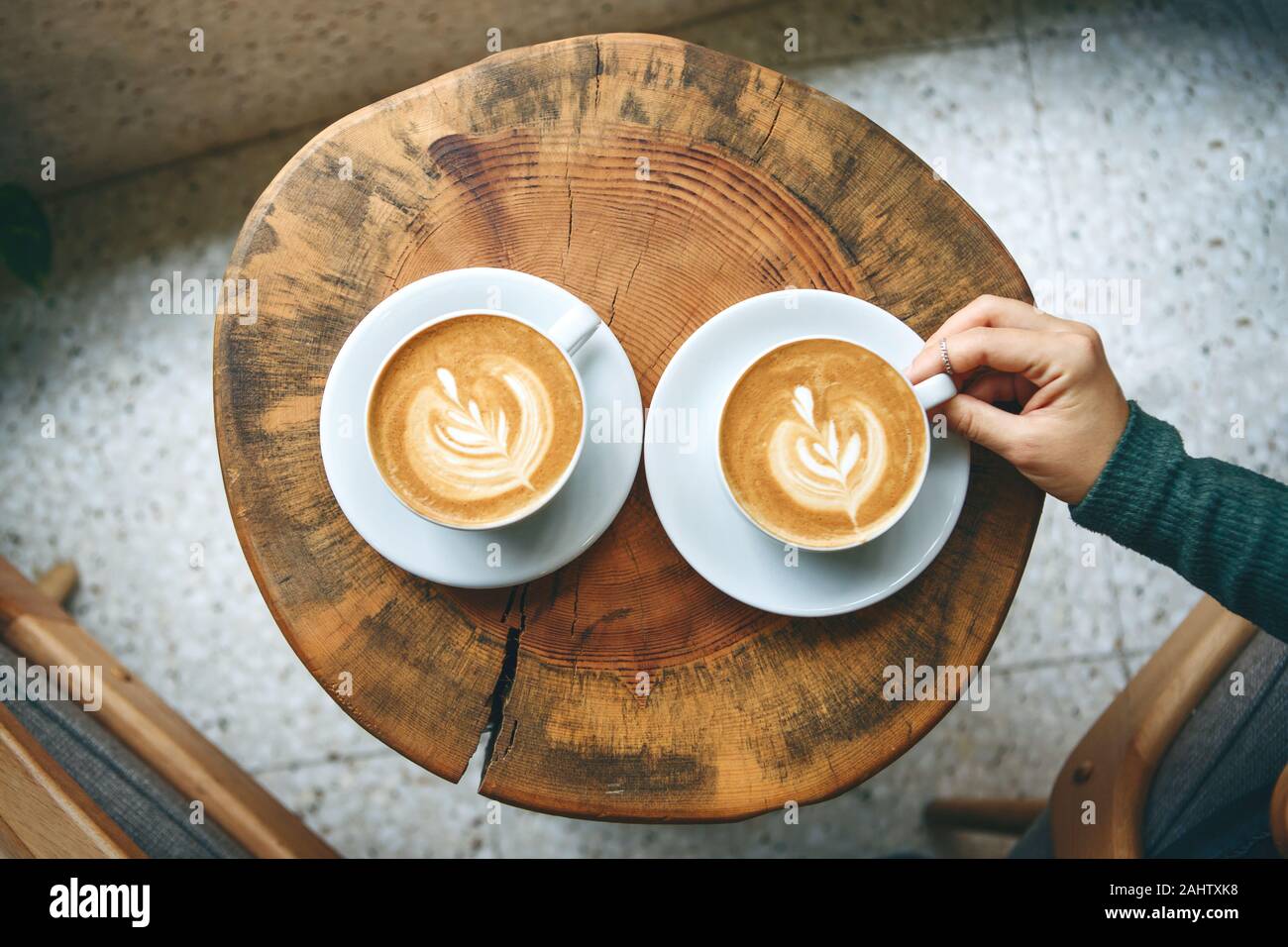 Zwei Tassen aromatischen Kaffee Cappuccino oder Latte auf einer hölzernen Tisch. person hält eine Schale mit der Hand. Konzept der Sitzung oder Entspannen. Lecker morgen Getränke. Stockfoto