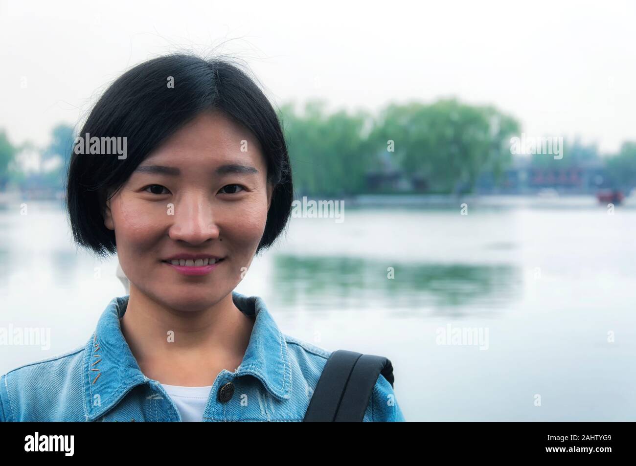 Eine chinesische Frau lächelnd vor Qianhai See in Hutong in der landschaftlich reizvollen Gegend von Beijing China an einem bewölkten Tag. Stockfoto