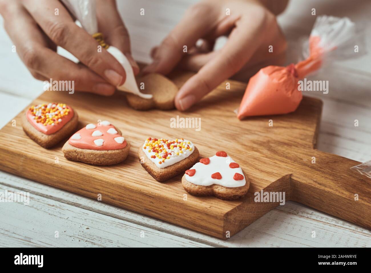 Dekoration Lebkuchen Kekse mit Zuckerguss. Frau Hände Cookies in Form von Herzen schmücken, Nahaufnahme Stockfoto