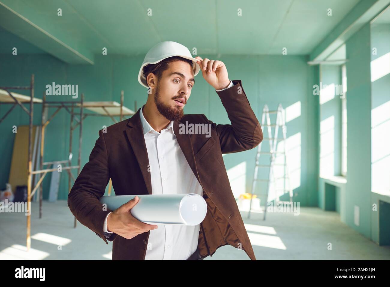 Builder Vorarbeiter in einem weißen Helm im Schock auf einer Baustelle im Innenbereich überrascht Stockfoto