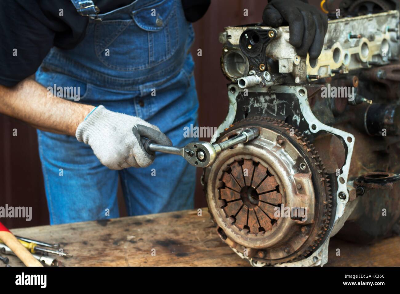 Kfz-Mechaniker bei der Arbeit Handschuhe schraubt die Kupplung vom Motorblock während der Reparatur in der Werkstatt. Stockfoto