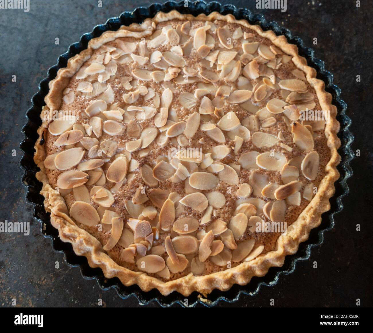 Ein hausgemachtes, frisch gebackene Bakewell tart garniert mit gerösteten Mandeln kühlt in der Backform auf ein Backblech. Stockfoto