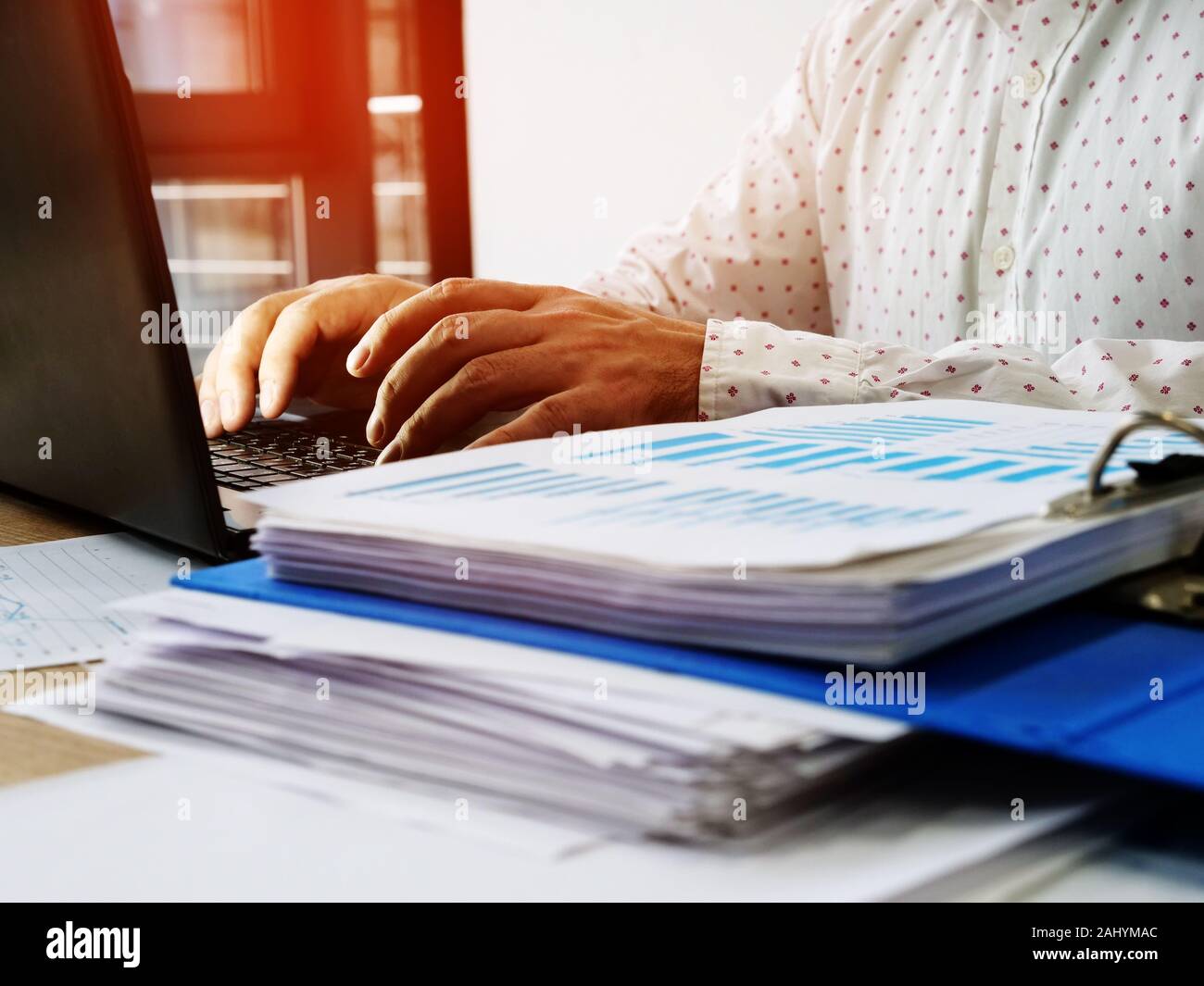 Ein Mann arbeitet an einem Computer im Büro. Stapel der finanziellen Leistung Papiere. Stockfoto