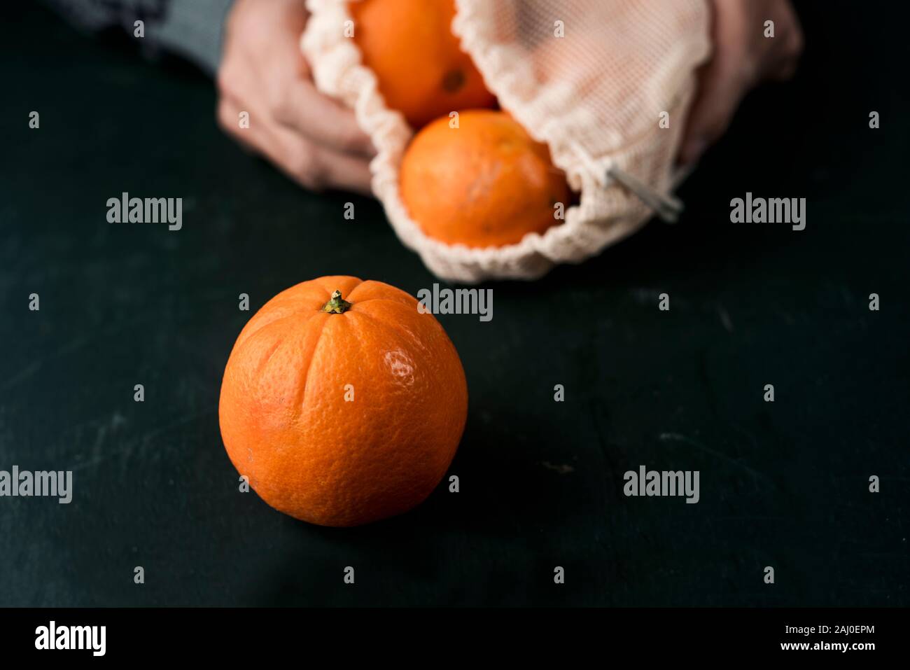 Nahaufnahme von einem Mann mit einem Textilen wiederverwendbaren Netzbeutel, verwendet, um Lebensmittel in loser Schüttung, voll von Orangen, als Maßnahme zur Verringerung der Umweltverschmutzung aus Kunststoff zu kaufen Stockfoto