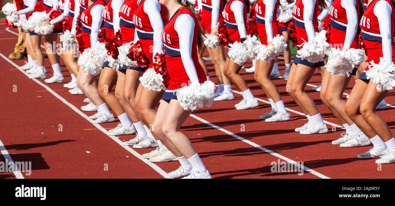 Ein High School Cheerleading Team ist auf einem roten Anschluss synchronisiert, während Sie für die Fans furing ein Fußballspiel. Stockfoto