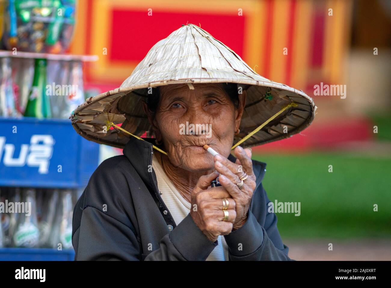 Asiatische Frau Verhalten eine kegelförmige Hut zündet sich eine Zigarette mit einem Feuerzeug Stockfoto