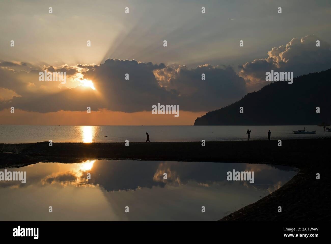 Wundervoller Sonnenaufgang, Sonnenstrahlen und Touristen am Strand von Adrasan Provinz Antalya in der Türkei. Es gab einen kleinen Teich am Strand mit Reflexionen. Stockfoto