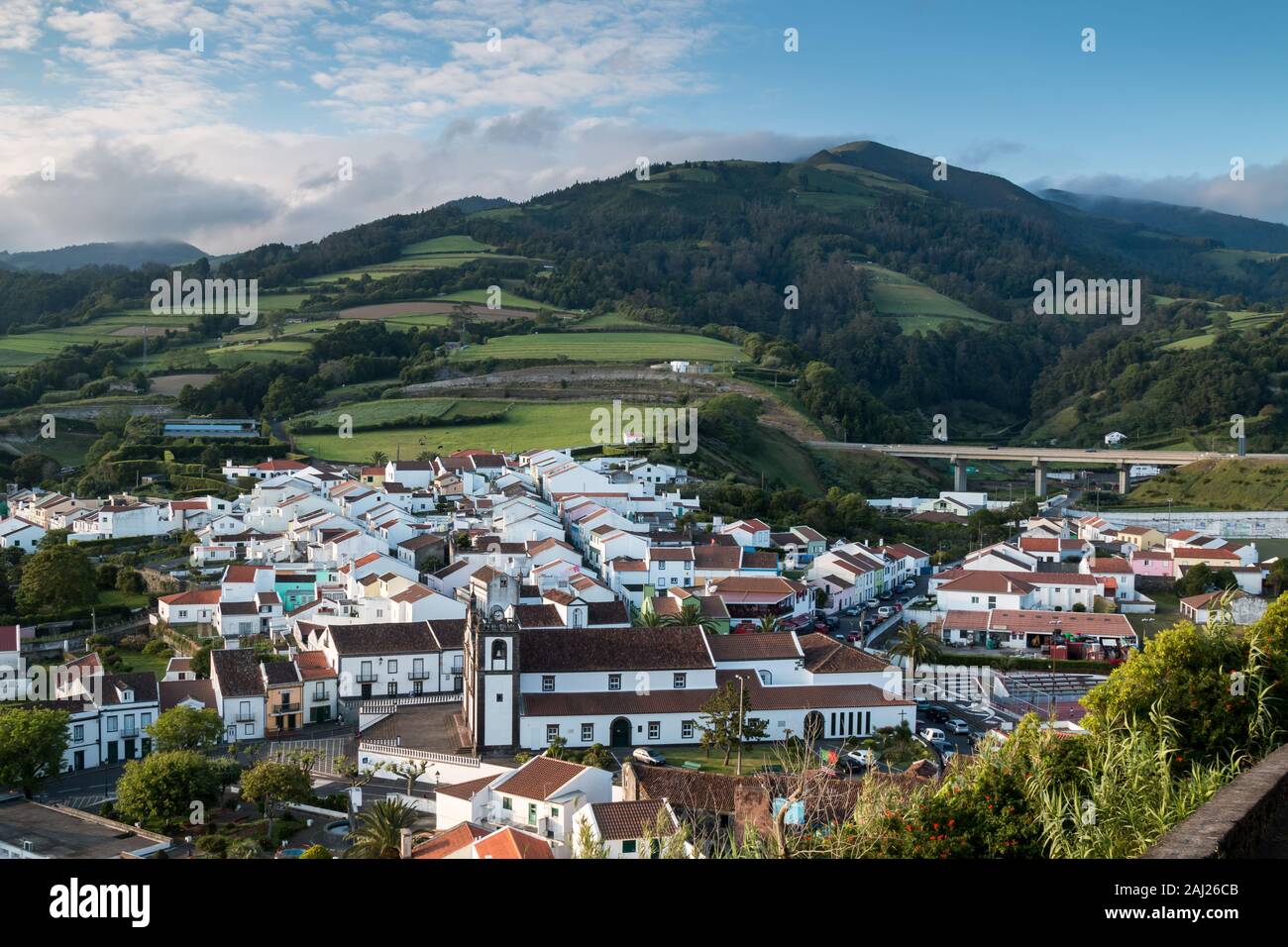 Blick auf die Stadt in einem Tal, umgeben von Feldern und Wiesen umgeben. Berg mit Bäumen im Hintergrund. Bewölkt Abend Himmel. Agua de Pau, Sao Miguel, Azor Stockfoto