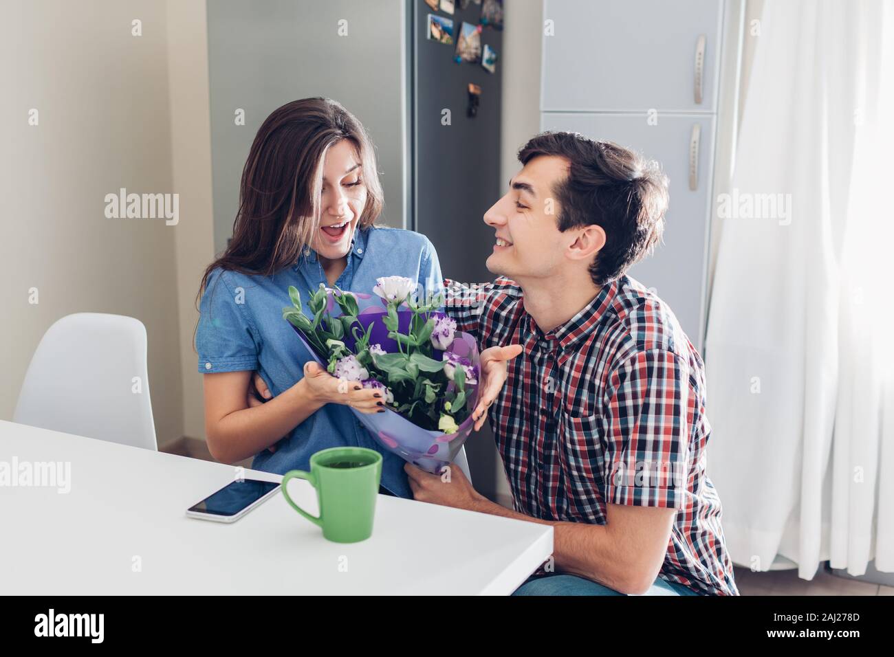 Mann gifting Blumenstrauß zu seiner Freundin auf Küche zu Hause. Valentines Tag romantische Überraschung. Glückliches Paar in der Liebe Stockfoto