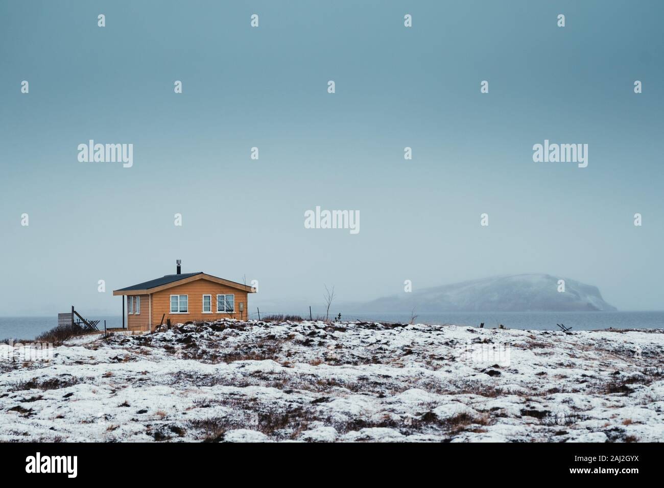 Isolierte kleine hölzerne Hütte im Winter Island mit Blick auf den See und die Berge im Hintergrund. Orange und teal Foto Stockfoto